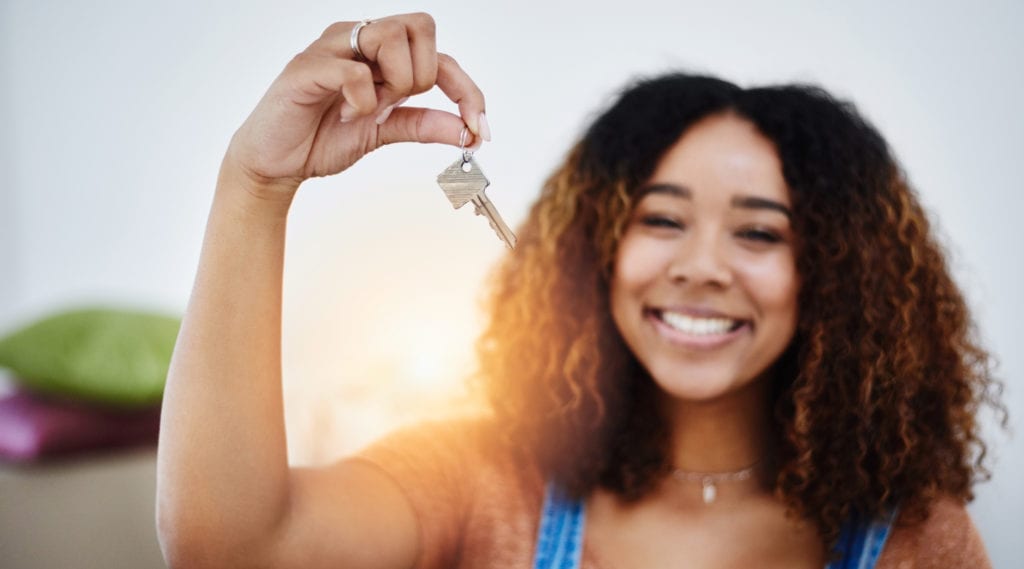Young woman smiling and holding the keys to her first apartment.
