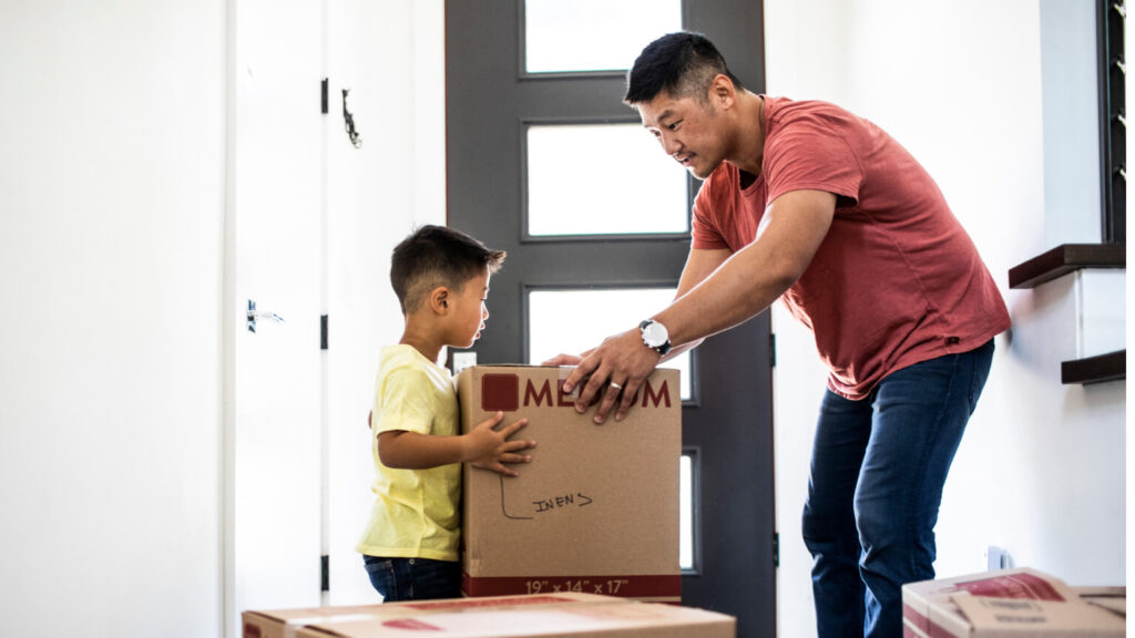 Father and son lifting moving boxes at new home