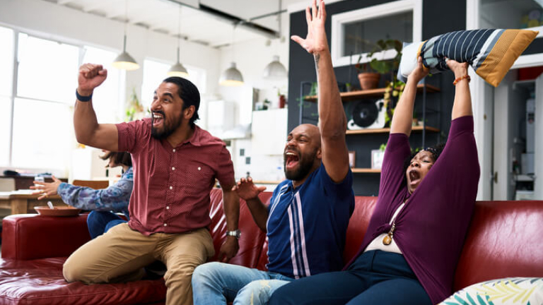 Friends watching TV at home and cheering with arms raised